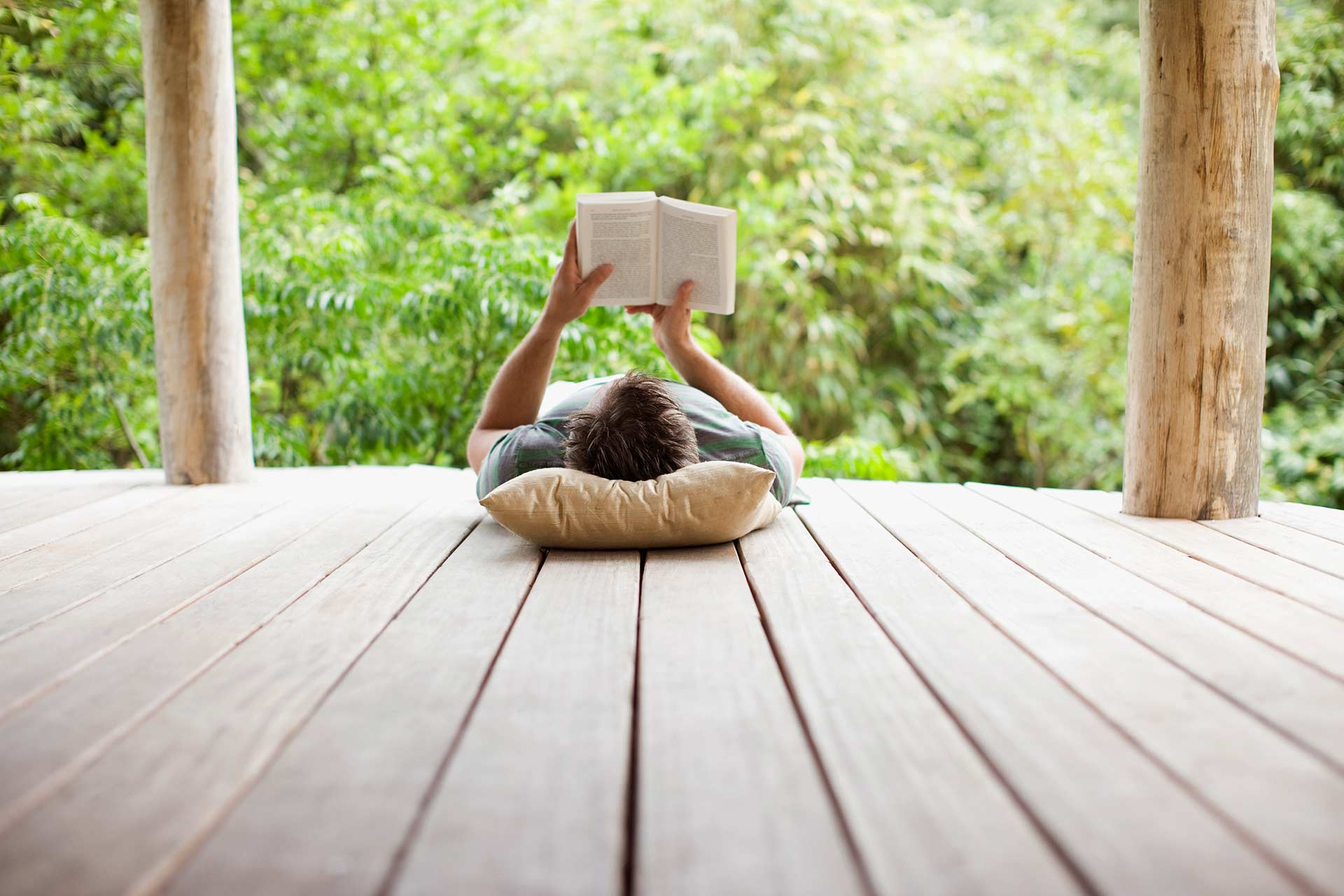 Mann entspannt mit Buch auf Terrasse